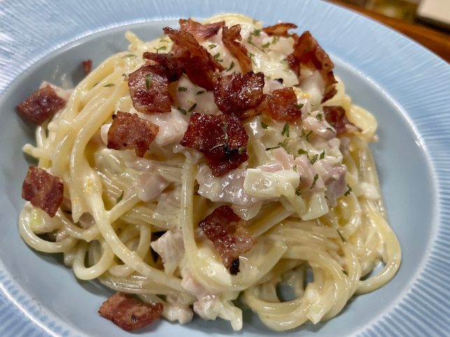 A plate of spaghetti with bacon and sauce